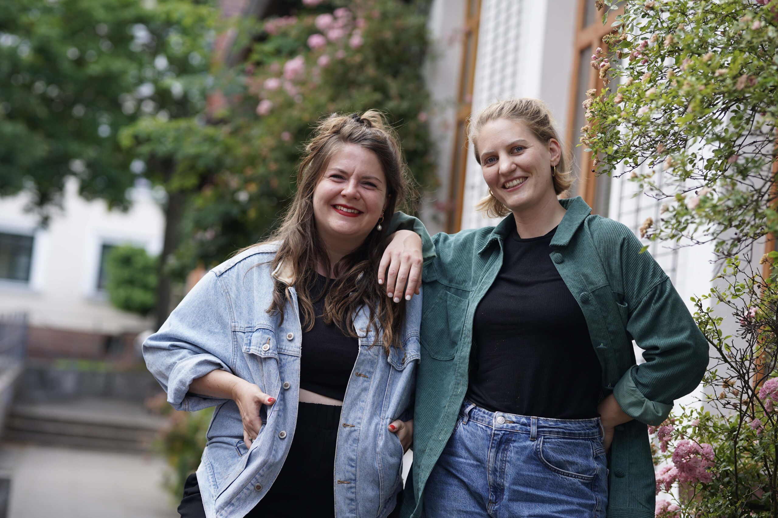 Zwei Frauen in bunten Hemden lehnen aneinander und lachen in die Kamera.