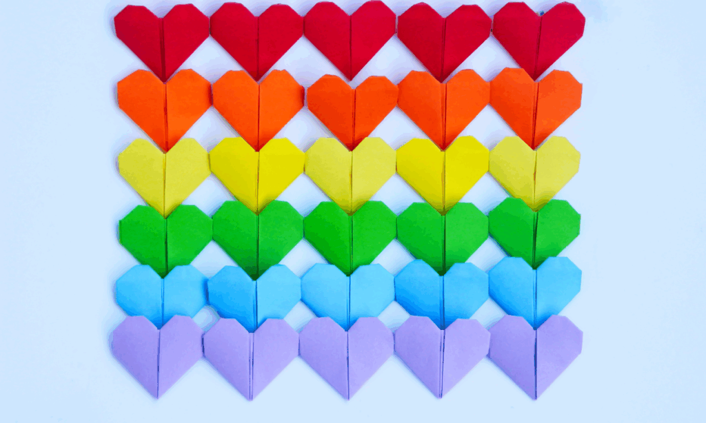 Kleine Papierherzen in Regenbogenfarben liegen auf einem hellblauen Hintergrund