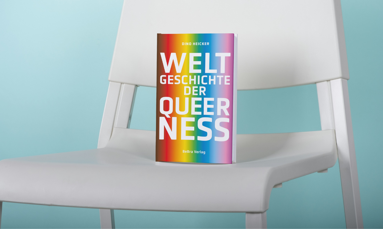 Das regenbogenfarbene Buch ist auf einem weißen Stuhl platziert. Der Hintergrund ist blau.