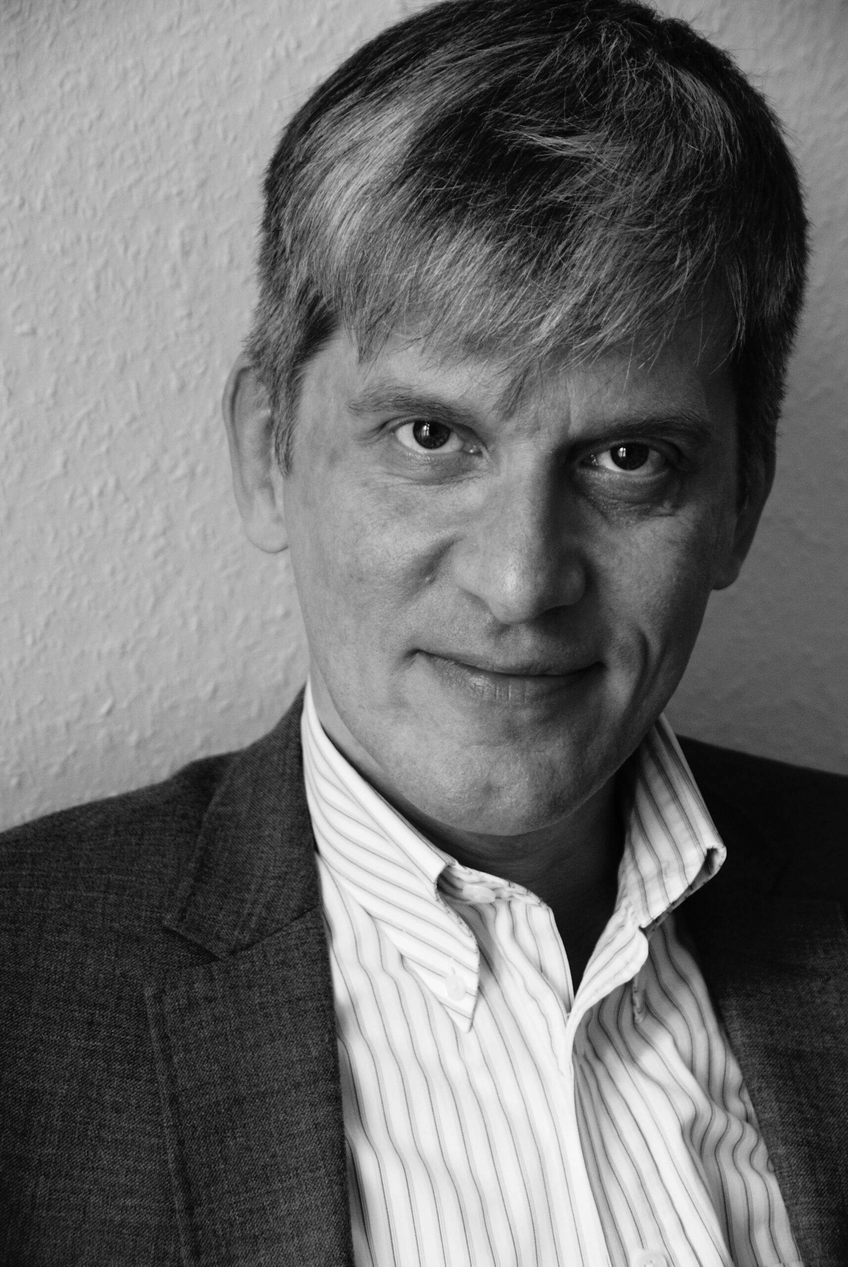 Das schwarzweiß Portrait zeigt, wie der Autor in die Kamera schaut. Er hat graue Haare und trägt ein Hemd.